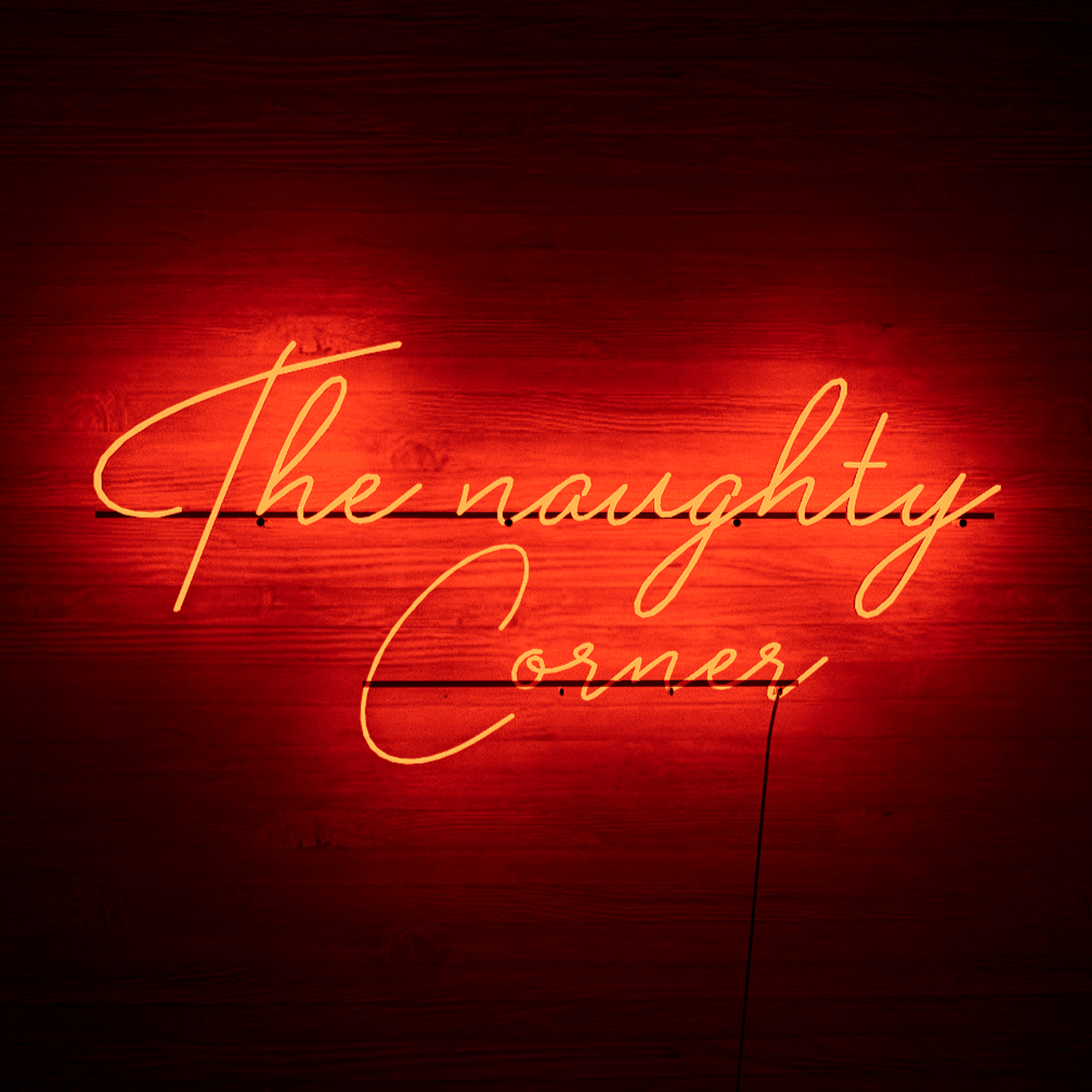 Dark night lit red neon lights hanging on the wall-The Naughty Corner